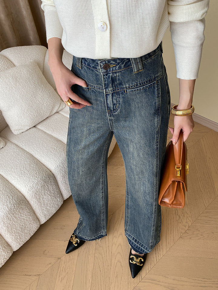 Frau in blauer Jeans und weißem Pullover, hält braune Ledertasche, modische Schuhe.