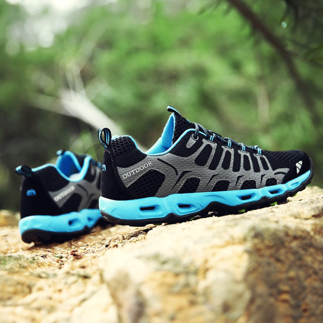 Schwarze Outdoor-Schuhe mit blauen Sohlen auf Felsen, atmungsaktiv, ideal für Wandern.