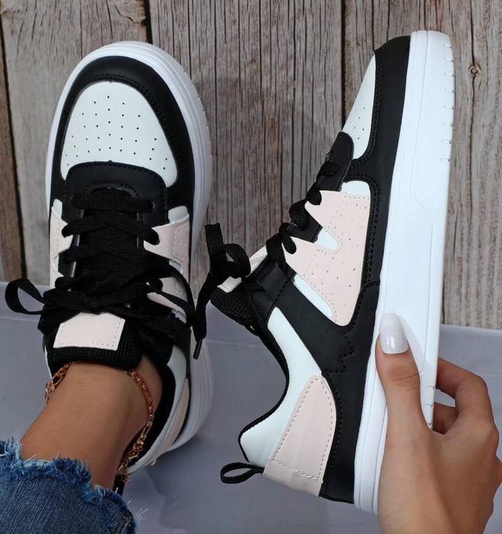 Schwarz-weiße Sneaker mit rosa Akzenten, Damenmode, Freizeitschuhe, Holz-Hintergrund.