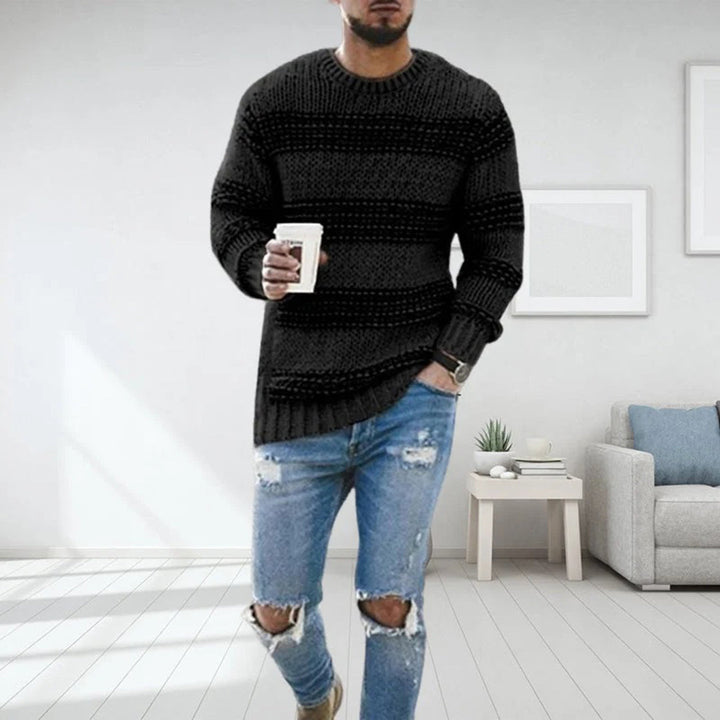 Mann in schwarzem Strickpullover und zerrissenen Jeans, hält Kaffeetasse, modernes Wohnzimmer.
