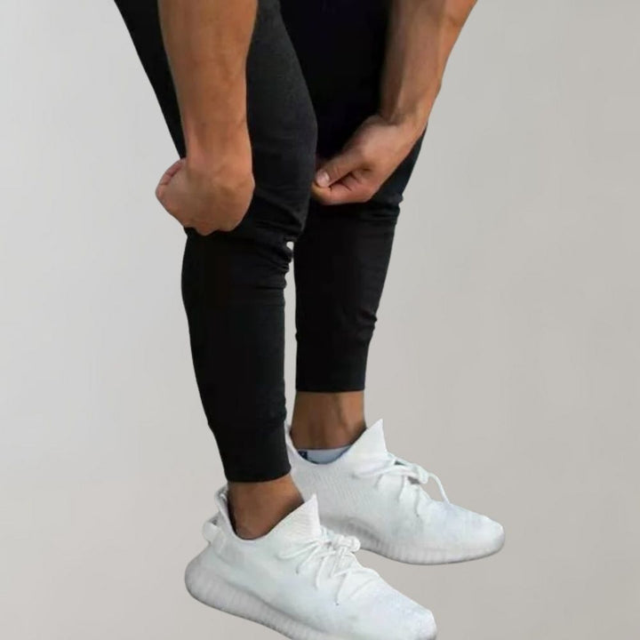 Mann in schwarzer Jogginghose und weißen Sneakers, sportlich, modern, bequem.