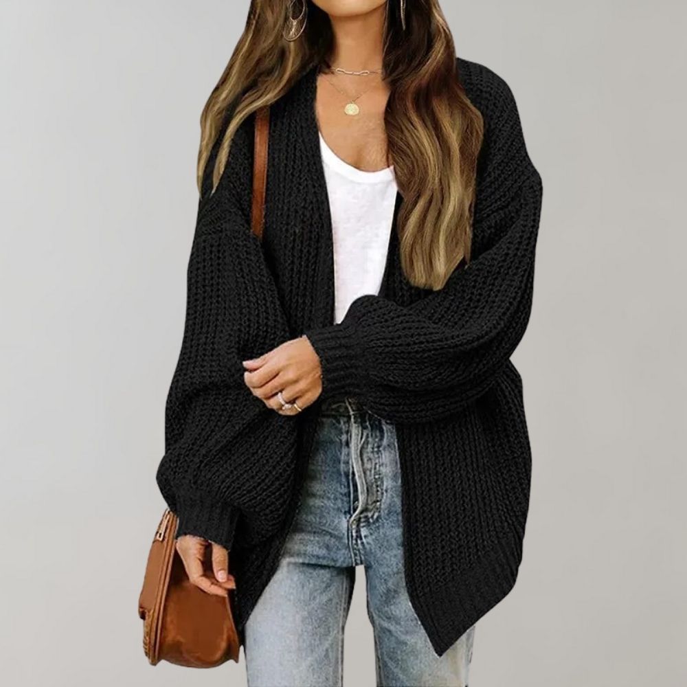 Frau in schwarzem Strickcardigan, weißem Top, Jeans, brauner Tasche.