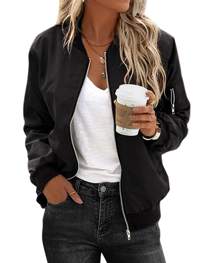 Frau in schwarzer Bomberjacke, weißem T-Shirt, hält Kaffeebecher, lässiger Streetstyle.