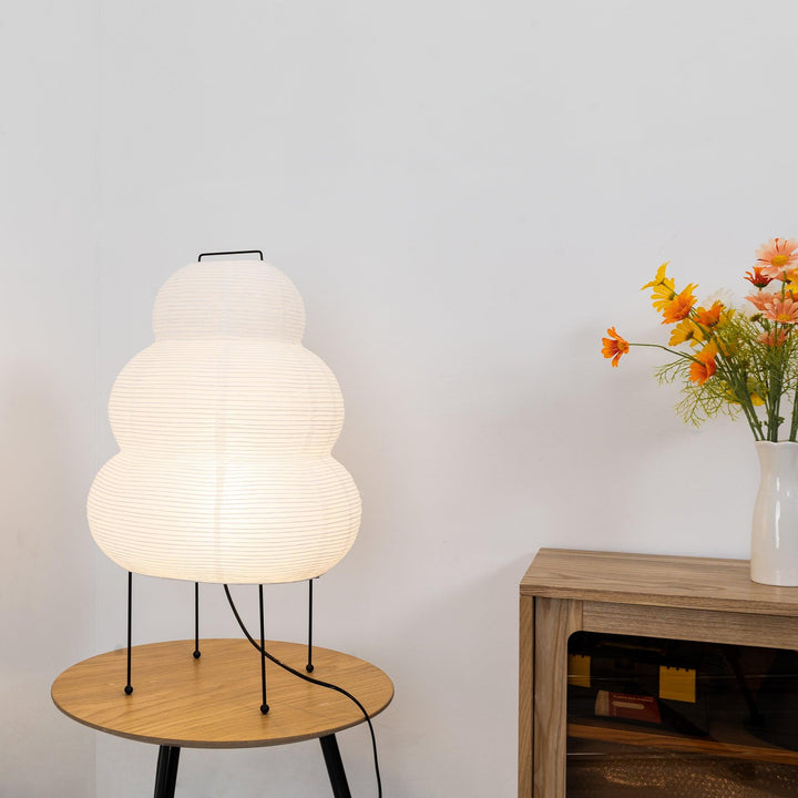 Weiße Papierlampe auf Holztisch, moderne Inneneinrichtung, neben Vase mit Blumen.