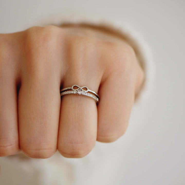 Damenhand mit silbernem Unendlichkeitsring und Diamant, eleganter Schmuck, Nahaufnahme.