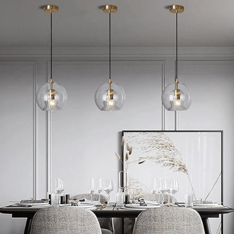 Drei moderne Glas-Pendelleuchten über Esstisch, goldene Akzente, elegantes Esszimmer-Design.