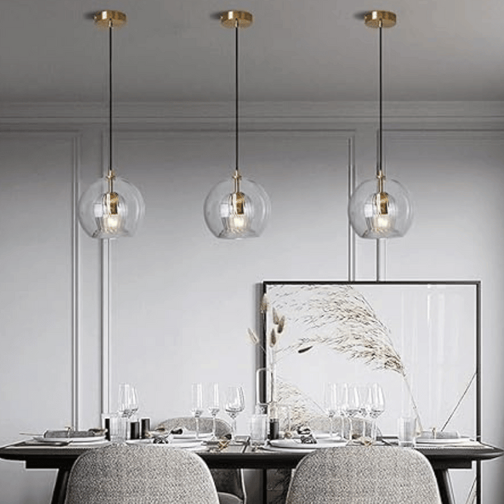 Drei moderne Glas-Pendelleuchten über Esstisch, goldene Akzente, elegantes Esszimmer-Design.