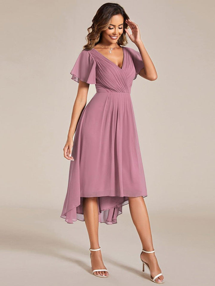 Model in a dusty pink asymmetrical chiffon dress with flutter sleeves and a high-low hem, worn with white strappy sandals. 62
