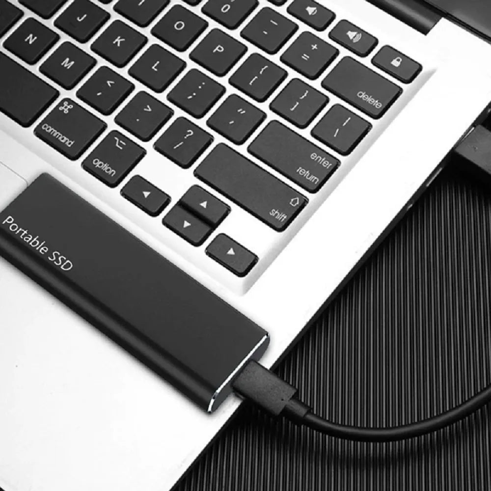 Černý externí disk ležící na klávesnici notebooku a připojený černým kabelem, detail při používání. 5