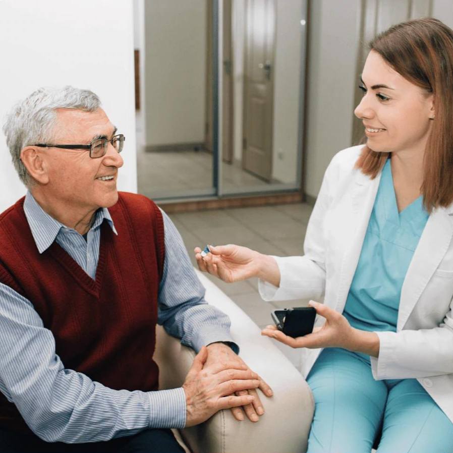 Älterer Mann erhält Hörgerät von Ärztin in Klinik, Hörgeräteanpassung, Gesundheitsversorgung.