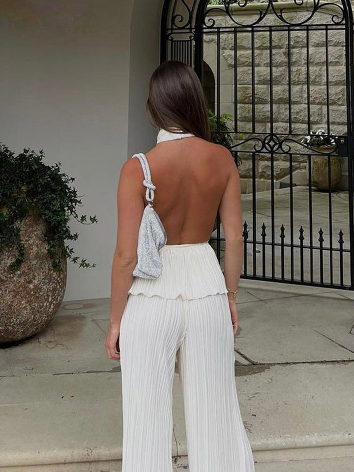 Frau in weißem, rückenfreiem Jumpsuit vor schmiedeeisernem Tor, eleganter Sommerlook.