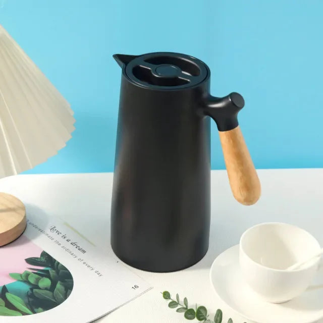 Schwarze Thermoskanne mit Holzgriff auf Tisch, skandinavisches Design, moderne Küche.