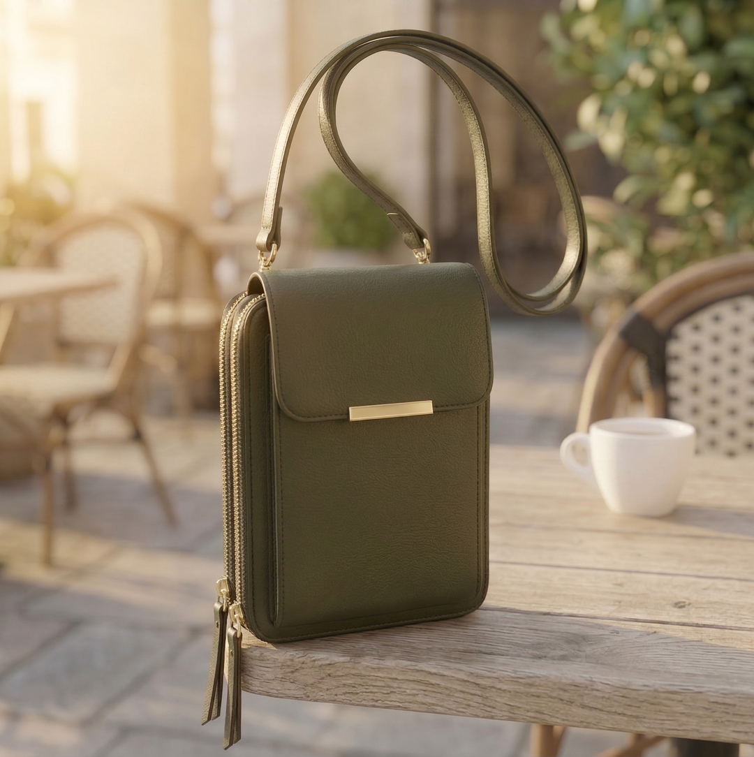 Olivově zelená varianta crossbody peněženky se zlatým zipem a dlouhým popruhem na dřevěném stole před kavárnou. 5