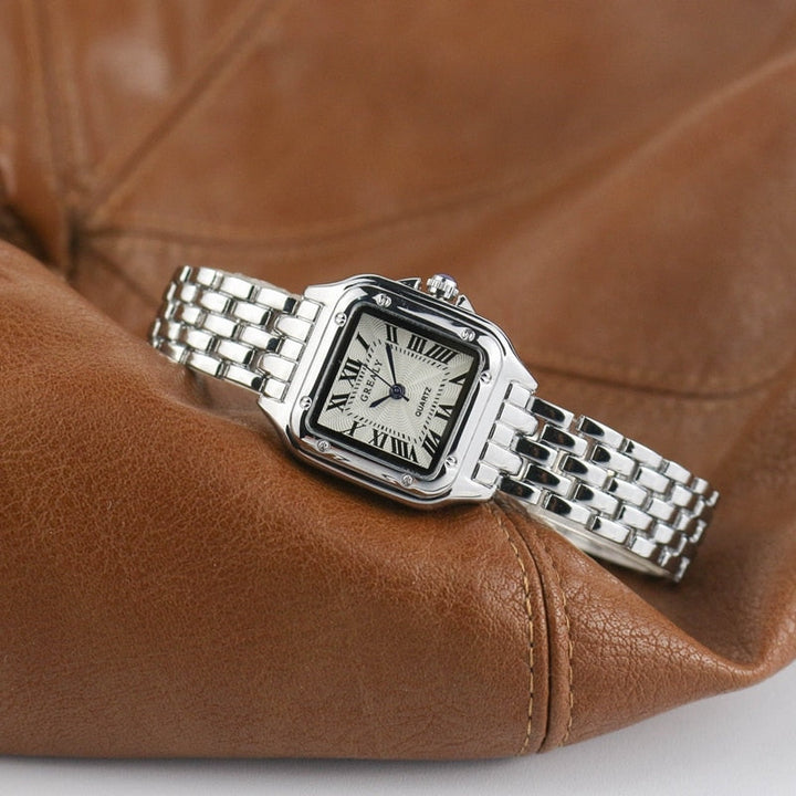 Silberne Armbanduhr mit römischen Ziffern auf braunem Lederhintergrund, elegantes Design.