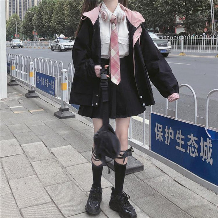 Mädchen in Schuluniform mit schwarzer Jacke und rosa Krawatte auf Gehweg in der Stadt.