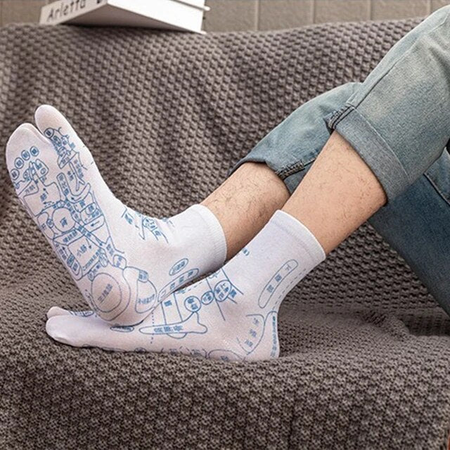 Weiße Akupressur-Socken mit blauen Reflexzonen-Diagrammen auf grauem Sofa.