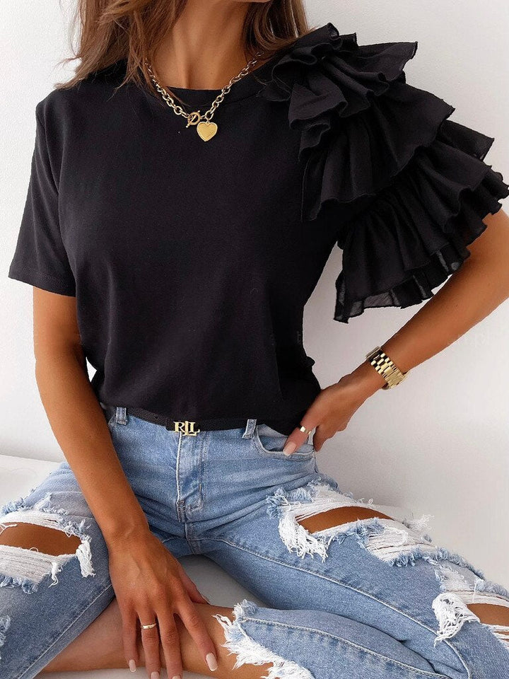 Frau in schwarzem Rüschen-Top und zerrissenen Jeans, modisches Outfit, Goldkette, Armbanduhr.