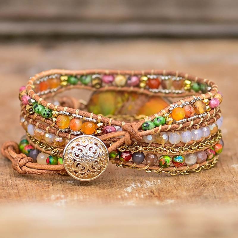 Mehrfarbiges Wickelarmband mit Edelsteinen und goldfarbenem Knopf auf Holzoberfläche.