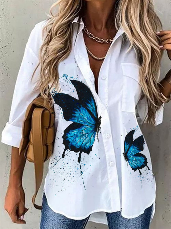 Frau in weißer Bluse mit blauem Schmetterlingsdruck, Jeans, braune Tasche, modisch, lässig.