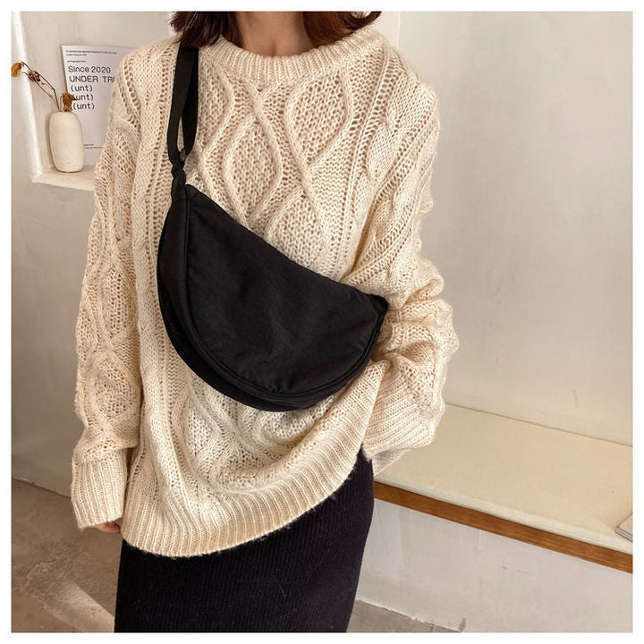 Frau mit cremefarbenem Strickpullover und schwarzer Umhängetasche in modernem Raum.