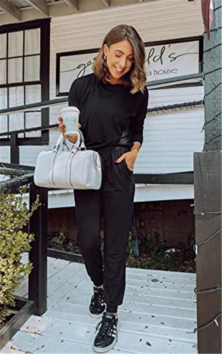 Frau in schwarzem Jumpsuit mit silberner Handtasche und Kaffee, lächelnd auf Veranda.
