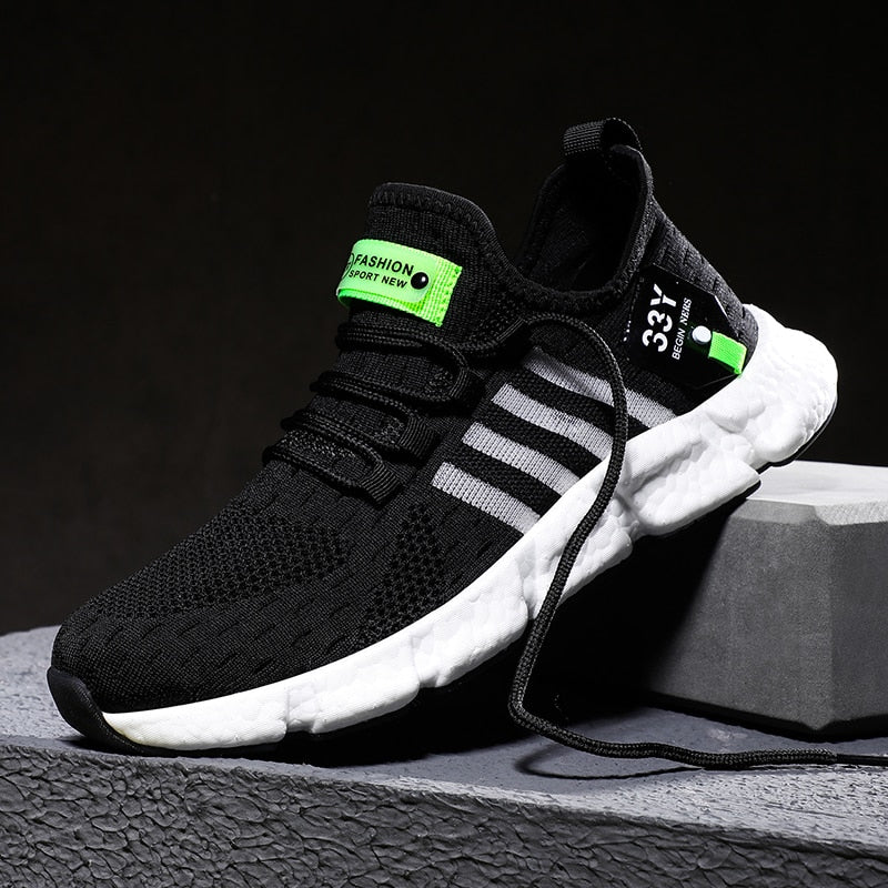 Schwarzer Sportschuh mit weißen Streifen, grünen Akzenten, atmungsaktivem Mesh-Obermaterial.