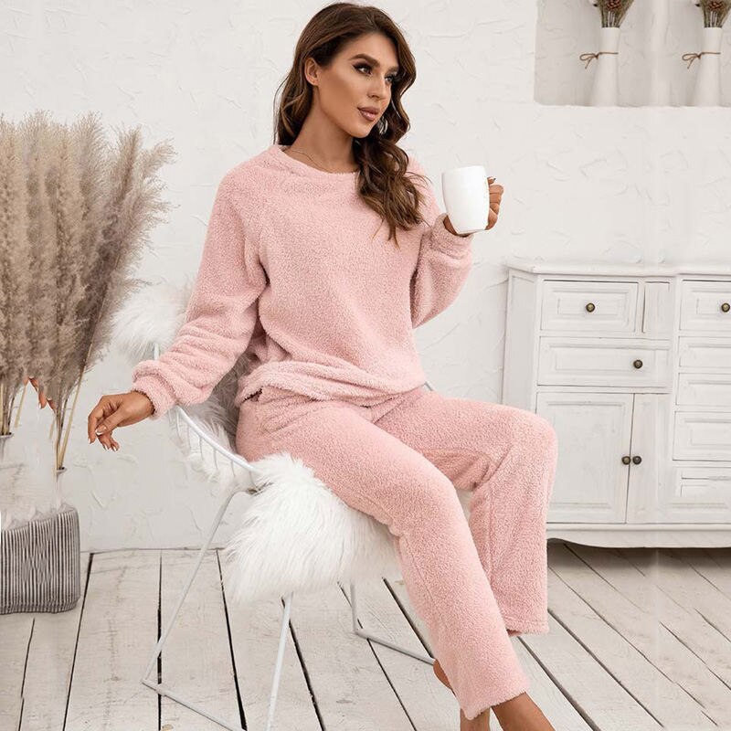 Frau in rosa Fleece-Pyjama mit Tasse, sitzt auf Stuhl, gemütliche Winterkleidung.