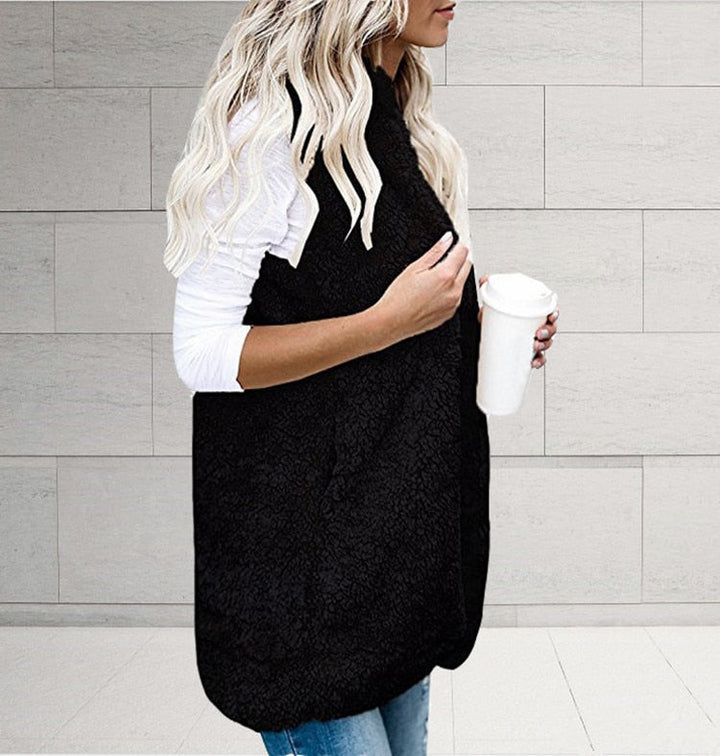 Frau in schwarzer Fleeceweste mit Kaffeebecher, weiße Bluse, blonde Haare, lässiger Stil.