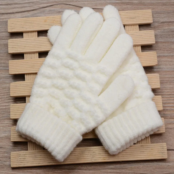 Weiße gestrickte Winterhandschuhe aus Wolle auf Holzunterlage, warm und weich.