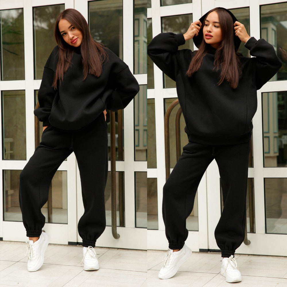 Frau in schwarzem Jogginganzug, Kapuzenpullover und Jogginghose, weiße Sneaker, lässige Mode.
