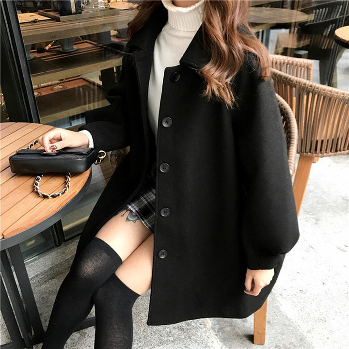 Frau in schwarzem Wollmantel, Rollkragenpullover, kariertem Rock, sitzt im Café.