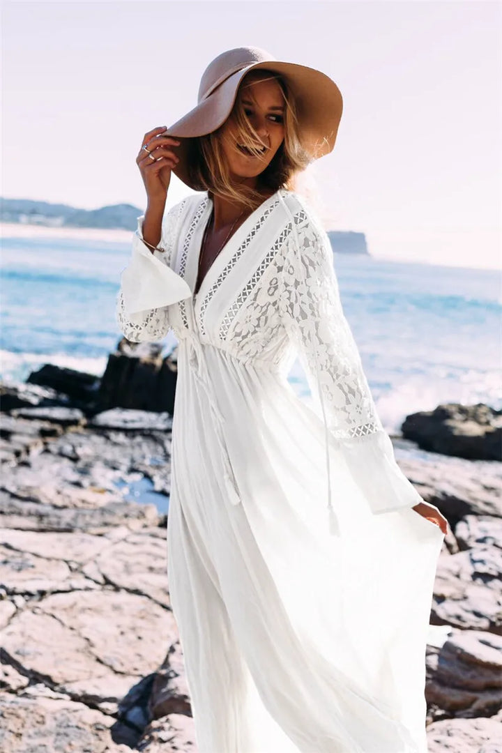 Frau in weißem Spitzenkleid am Strand, Sommerhut, Meereshintergrund, Boho-Mode.