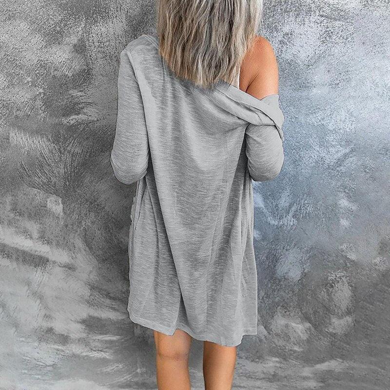 Frau in grauem, schulterfreiem Kleid vor grauer Wand, lässige Mode, Rückansicht.