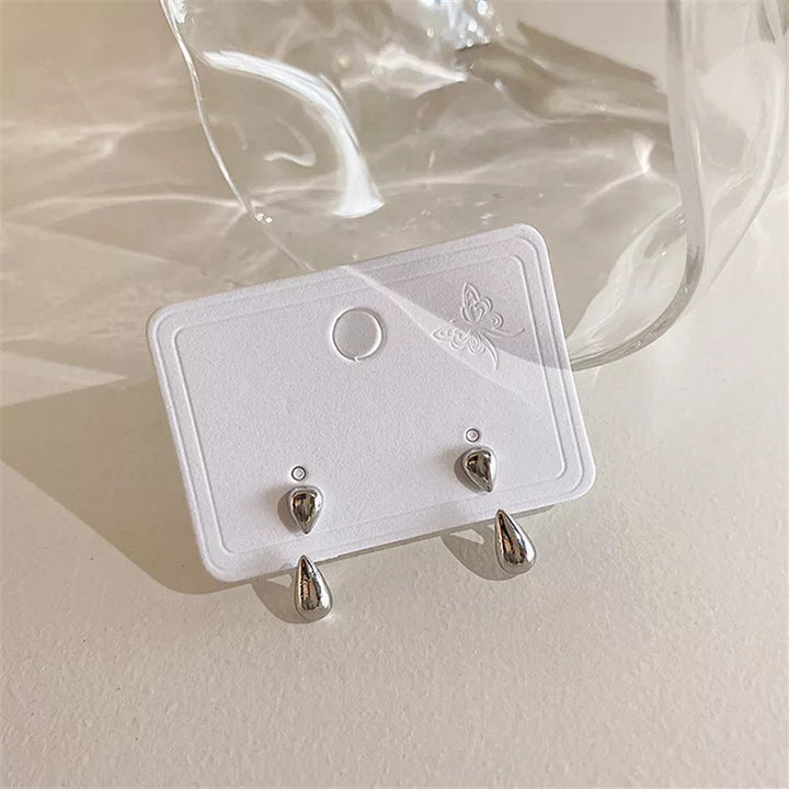 Silberne Tropfen-Ohrringe auf weißer Karte, minimalistisches Design, Schmuckaccessoire.