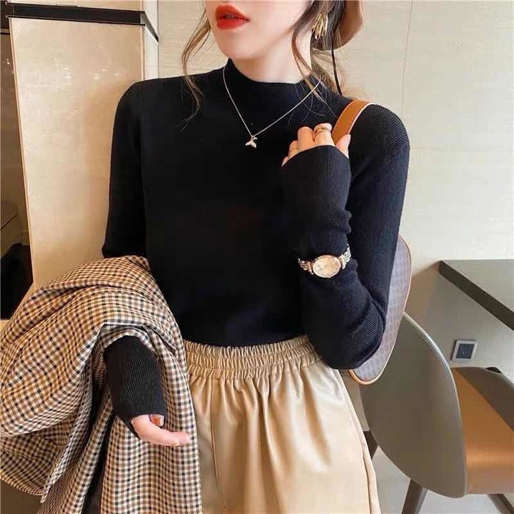 Frau in schwarzem Pullover und beiger Hose, trägt karierten Mantel und Armbanduhr.