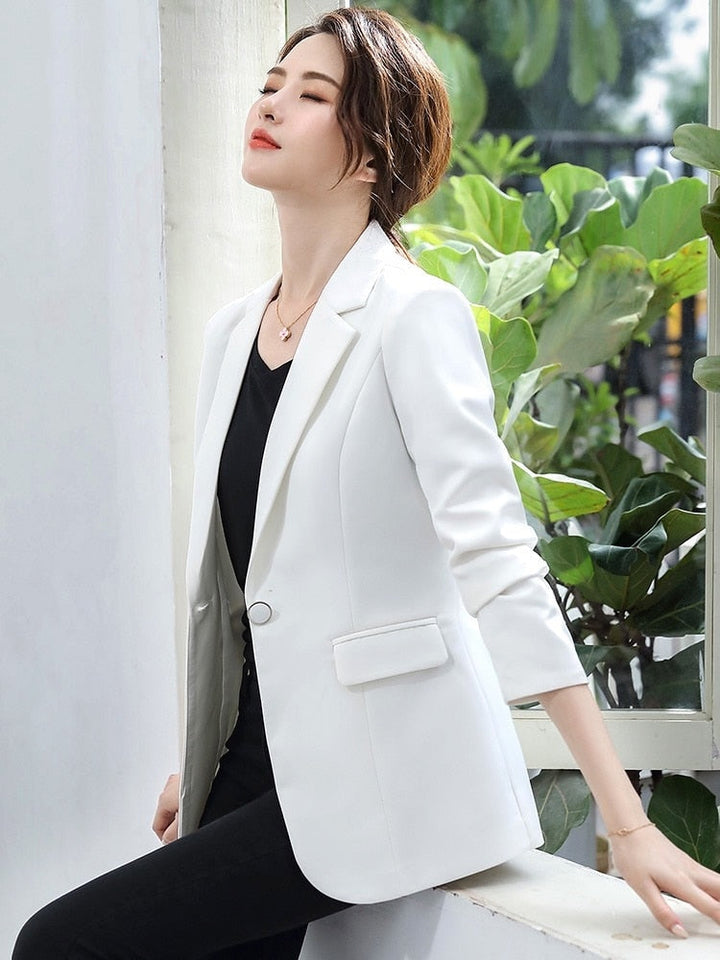 Frau in weißem Blazer, elegantes Outfit, Businessmode, vor Pflanzen, stilvoll und modern.