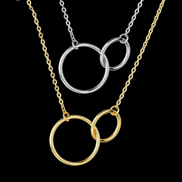 Zwei Halsketten mit ineinandergreifenden Ringen, eine in Silber, eine in Gold, auf schwarzem Hintergrund.