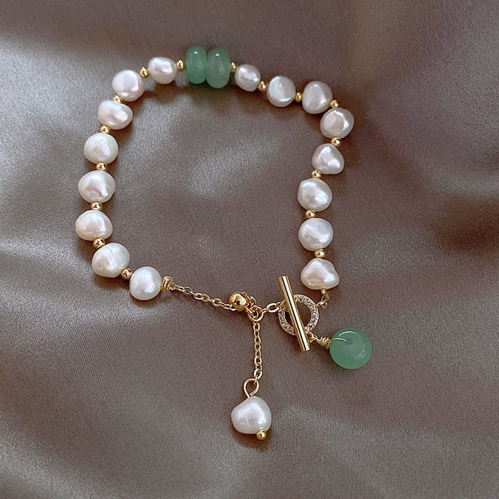 Perlenarmband mit grünen Jadesteinen, goldener Verschluss, eleganter Schmuck auf Seidenstoff.