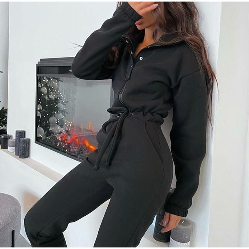 Frau in schwarzem Jogginganzug vor modernem Kamin, gemütliche Wintermode, Freizeitkleidung.