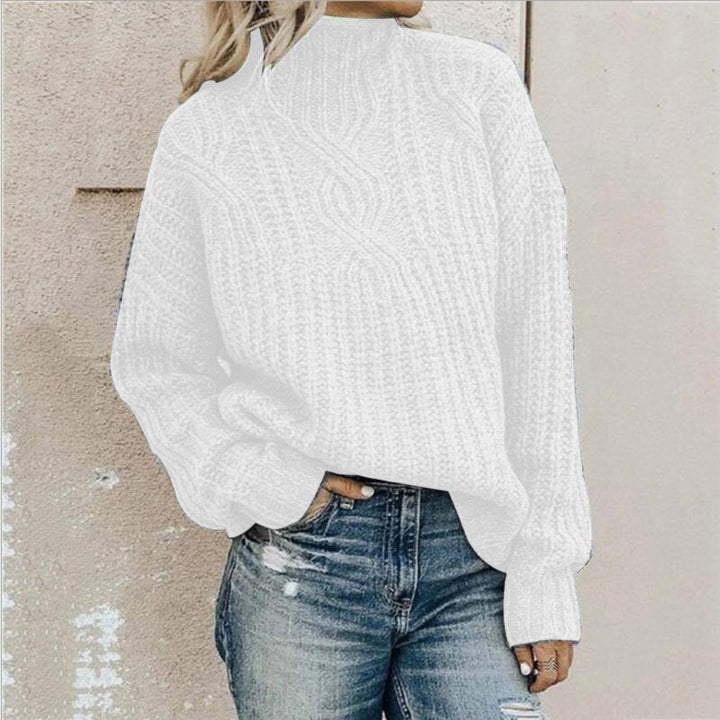 Frau in weißem Strickpullover und zerrissenen Jeans vor beiger Wand.