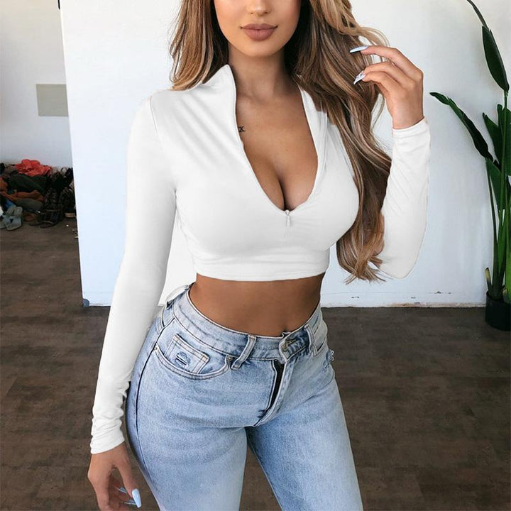 Frau in weißem Langarm-Crop-Top und blauer Jeans, modisch, lässig, Indoor-Hintergrund.