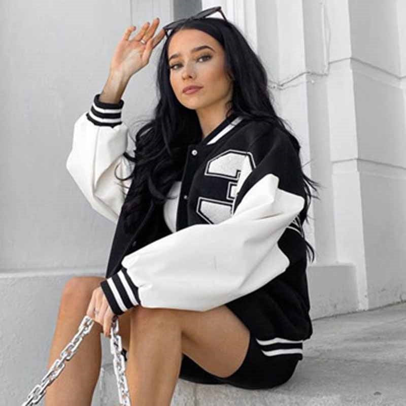 Frau in schwarz-weißer Collegejacke, sitzt auf Treppe, modisch, urbaner Stil.