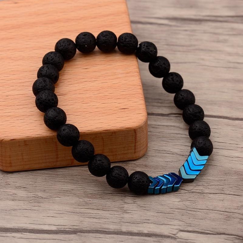 Schwarzes Lavastein-Armband mit blauen Pfeil-Perlen auf Holzuntergrund, modisches Schmuckstück.