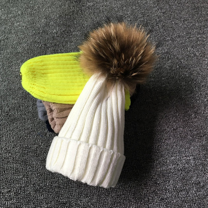 Weiße Strickmütze mit Fellbommel auf grauem Hintergrund, Wintermode Accessoire.