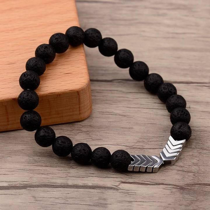 Schwarzes Lavastein-Armband mit silbernen Pfeil-Details auf Holzoberfläche, modisch, elegant.