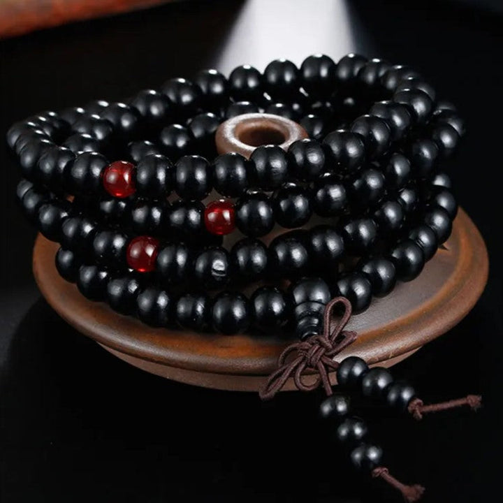 Schwarze Gebetskette aus Holz mit roten Perlen auf braunem Teller, spiritueller Schmuck.