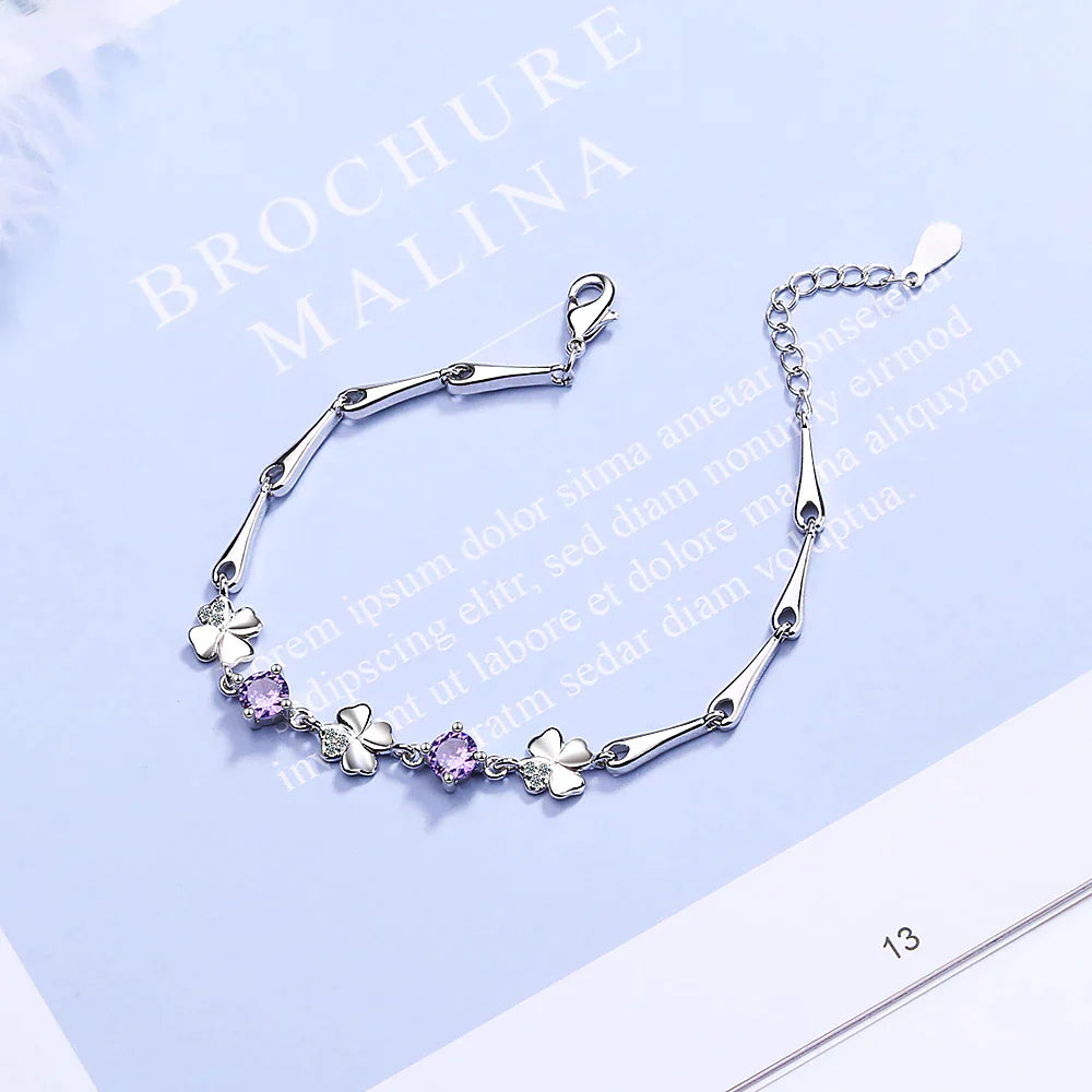 Silberarmband mit Kleeblatt- und lila Kristallanhängern, elegantes Schmuckdesign.