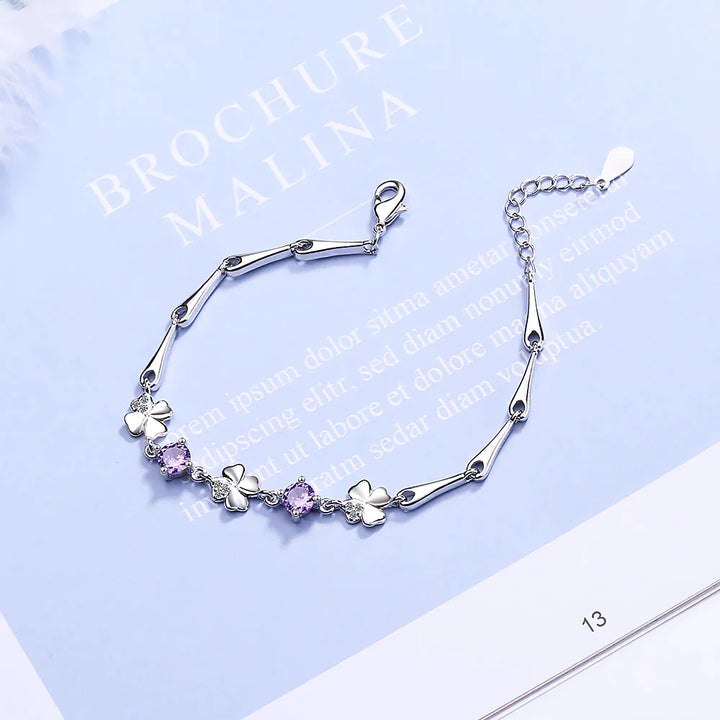 Silberarmband mit Kleeblatt- und lila Kristallanhängern, elegantes Schmuckdesign.