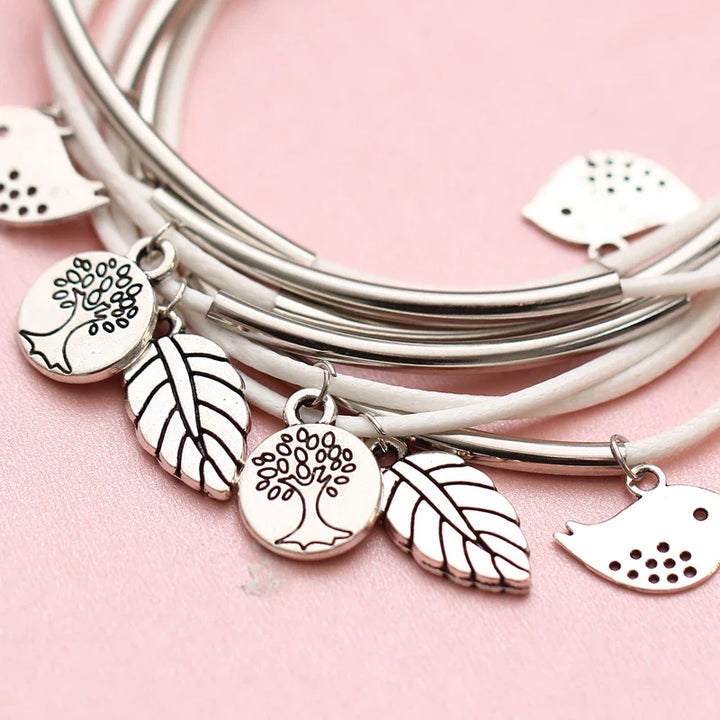 Silberne Armbänder mit Baum- und Blattanhängern auf rosa Hintergrund, Modeschmuck Accessoires.