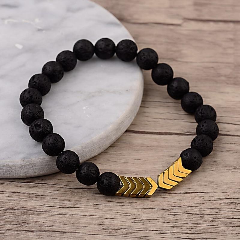 Schwarzes Lavastein-Armband mit goldenen Pfeil-Details auf Holz- und Marmorhintergrund.